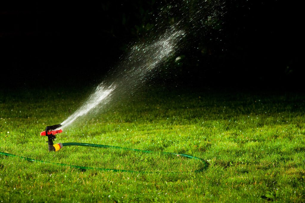 Lawn sprinkler spraying water over green grass at night
